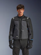 Alpinestars Cusco Drystar® Jacke, Motorrad-Tourenjacke, Schwarz und Dunkelgrau, Vorderansicht am Modell, mit Alpinestars-Logos auf Brust und Schultern, Drystar®-Branding am Ärmel, technisches Multi-Pocket-Design mit Belüftungsreißverschlüssen, kombiniert mit schwarzer Motorradausrüstung