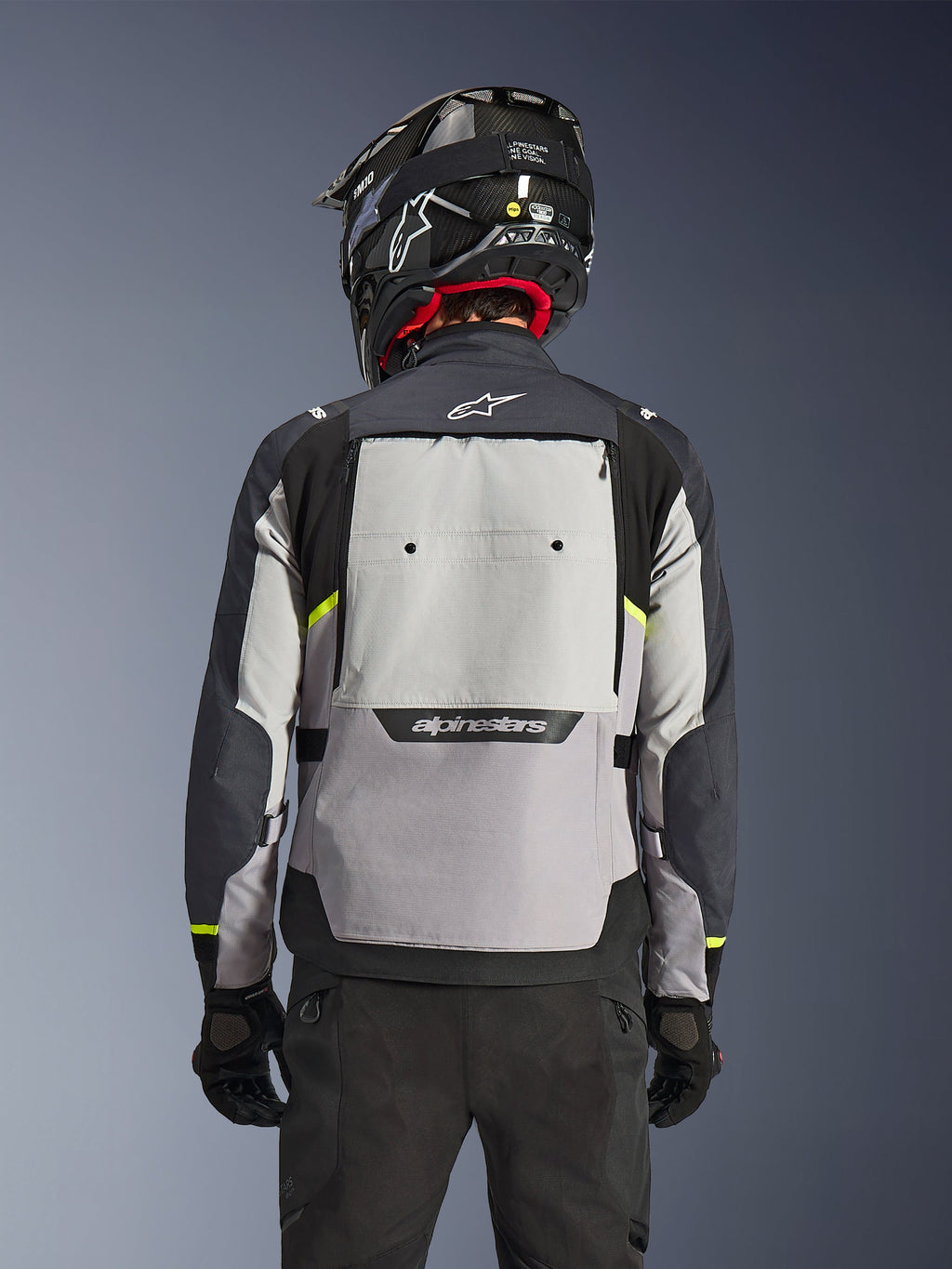 Alpinestars Cusco Drystar® Jacke, Rückansicht, Ice Gray, Mid Gray und Deep Gray, mit großem Belüftungspanel am Rücken und hochsichtbaren gelben Akzenten, kombiniert mit einem schwarzen Adventure-Helm und einer schwarzen Hose