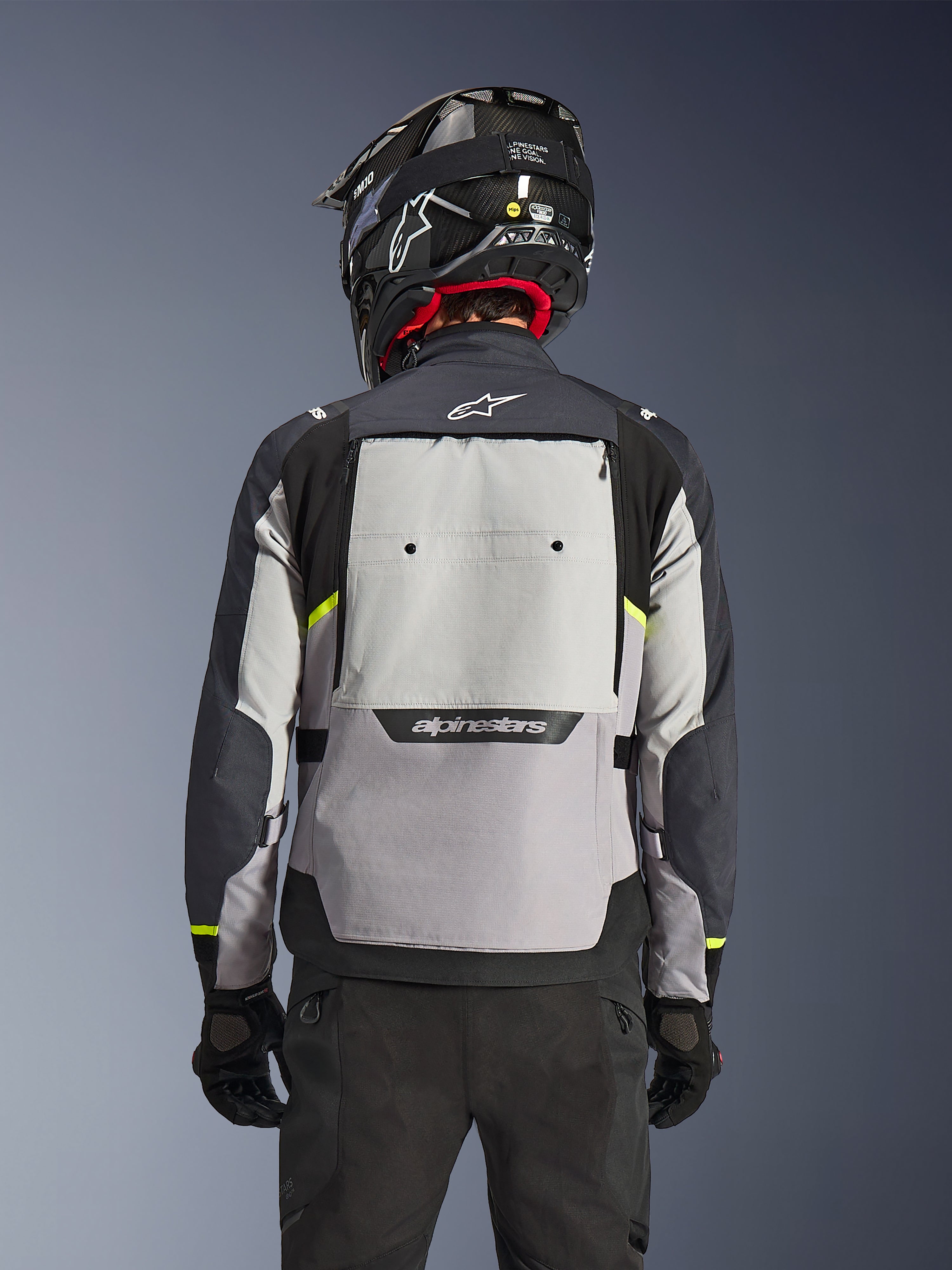 Alpinestars Cusco Drystar® Jacke, Rückansicht, Ice Gray, Mid Gray und Deep Gray, mit großem Belüftungspanel am Rücken und hochsichtbaren gelben Akzenten, kombiniert mit einem schwarzen Adventure-Helm und einer schwarzen Hose
