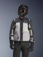 Alpinestars Cusco Drystar® Jacke, Adventure-Touring-Jacke, Ice Gray, Mid Gray und Deep Gray, mit mehrfarbigen Graupaneelen, Brustbelüftungen mit Reißverschluss und Alpinestars-Branding, getragen von einem Fahrer mit schwarzem Helm und Goggles.
