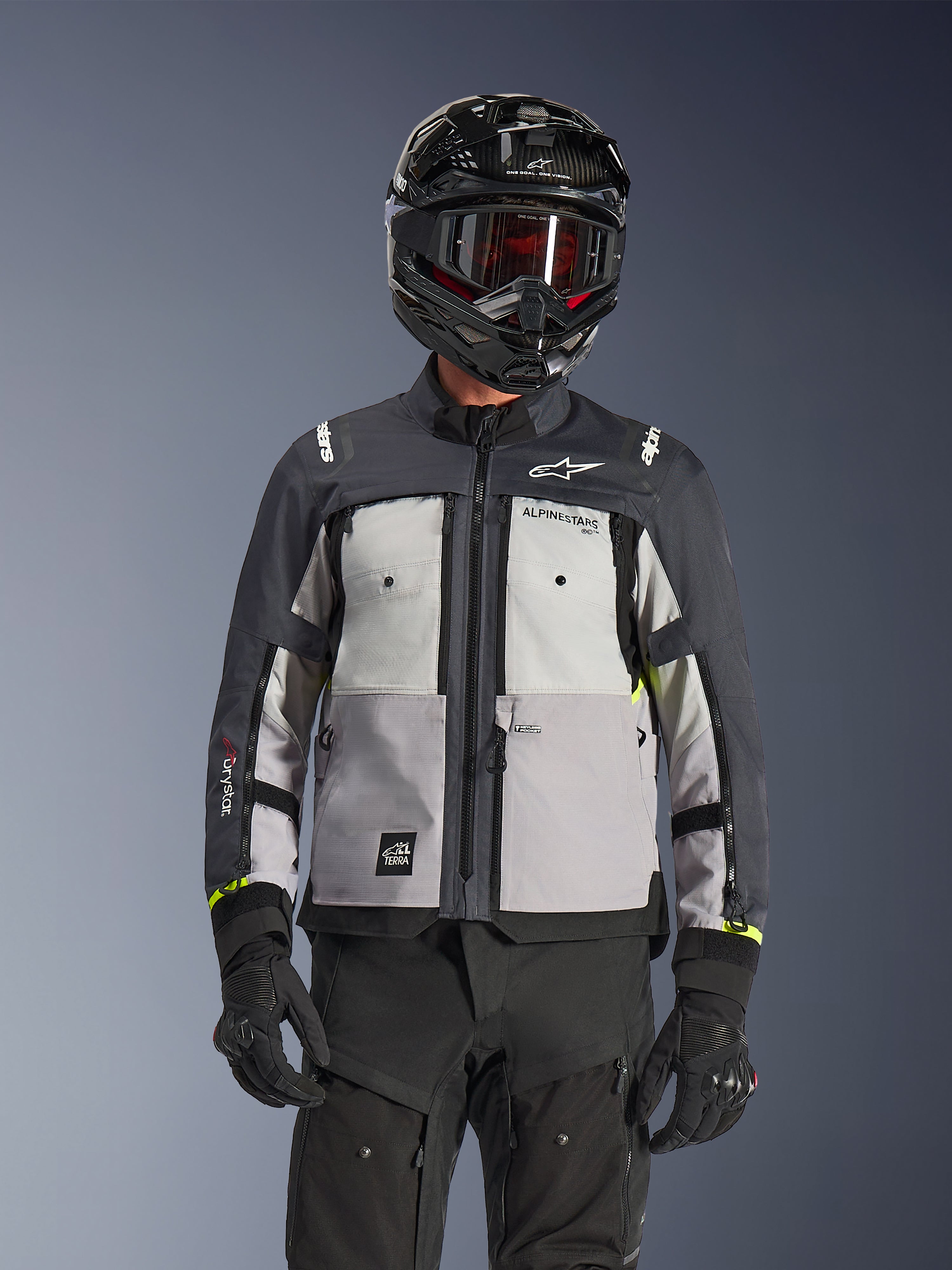 Alpinestars Cusco Drystar® Jacke, Adventure-Touring-Jacke, Ice Gray, Mid Gray und Deep Gray, mit mehrfarbigen Graupaneelen, Brustbelüftungen mit Reißverschluss und Alpinestars-Branding, getragen von einem Fahrer mit schwarzem Helm und Goggles.