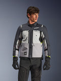 Alpinestars Cusco Drystar® Jacke, Adventure-Touren-Motorradjacke, Ice Gray, Mid Gray und Deep Gray, getragen von einem Modell mit schwarzer Hose und Handschuhen, mit einem mehrteiligen technischen Textildesign, Brusttaschen, 'Drystar'-Branding auf dem Ärmel und dezenten neongelben Akzenten an den Ärmelbündchen.