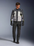 Alpinestars Cusco Drystar® Jacke in Ice Gray, Mid Gray und Deep Gray, getragen mit schwarzer Adventure-Motorradhose und Handschuhen, Textil-Adventure-Tourenjacke mit mehrfarbigen grauen Einsätzen und neongelben Akzenten, Studioaufnahme eines männlichen Models.