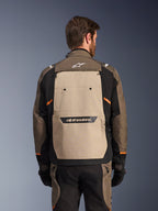Alpinestars Cusco Drystar® Jacke, Walnut Aluminum Black, Rückansicht, mit einem großen beigen Rückenpanel mit schwarzem Logo, orangefarbenen Akzenten, getragen mit passender Hose und Handschuhen, entwickelt für Adventure-Touring.