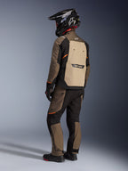 Alpinestars Cusco Drystar® Jacke, Adventure-Tourenjacke, Walnut Aluminum Black, Rückansicht mit beigem Rückenteil und orangefarbenen Akzenten, getragen mit passender Hose und schwarzem Carbon-Helm.