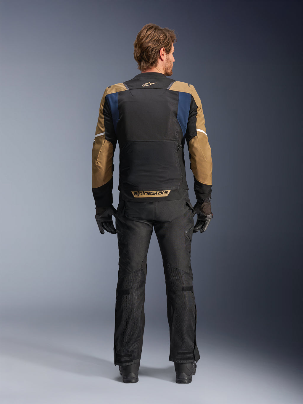 Alpinestars ST-2 Air Jacke in Tiefblau, Dunklem Khaki und Schwarz, Rückansicht am Modell mit großem Mesh-Rückenteil und khakifarbenen Ärmeln mit weißen Streifen, kombiniert mit schwarzer technischer Motorradhose und Handschuhen für Adventure-Touring.