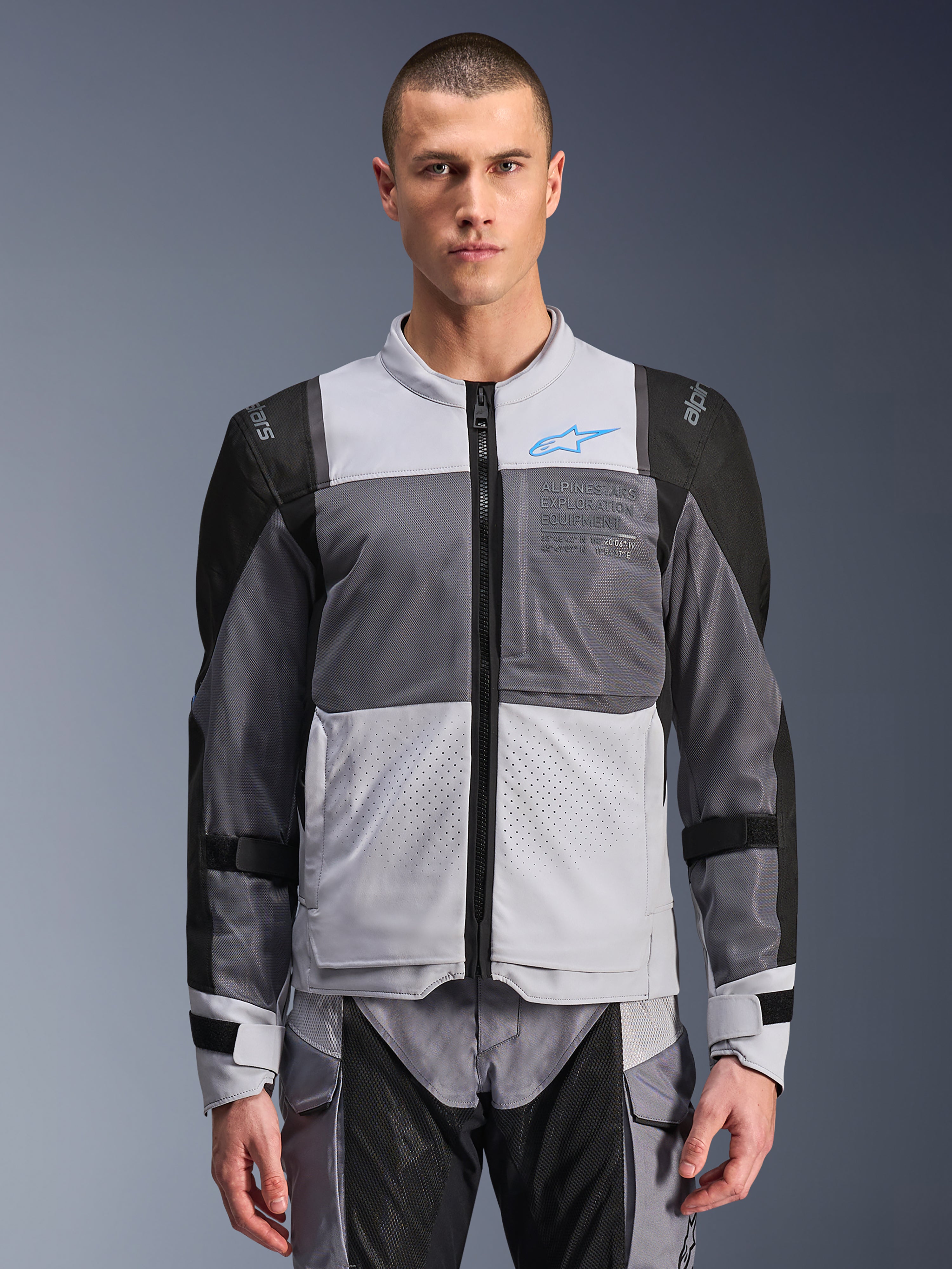 Alpinestars ST-2 Air Jacke, Motorradjacke für Herren, Eisgrau und Dunkelgrau mit schwarzen Akzenten, breite Mesh-Belüftungseinsätze, laserperforierte Vorderseite, blaues Alpinestars-Logo, Frontreißverschluss, getragen von einem Model mit passender Motorradhose