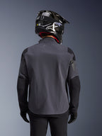 Maxdura Drystar®XF Laminierte Gepanzerte Jacke, Adventure-Motorradjacke, Dunkelgrau Schwarz, Rückansicht mit technischer Textilkonstruktion und verstärkten Panelen, getragen mit schwarzem Carbon-Helm, schwarzer Fahrhose und Handschuhen