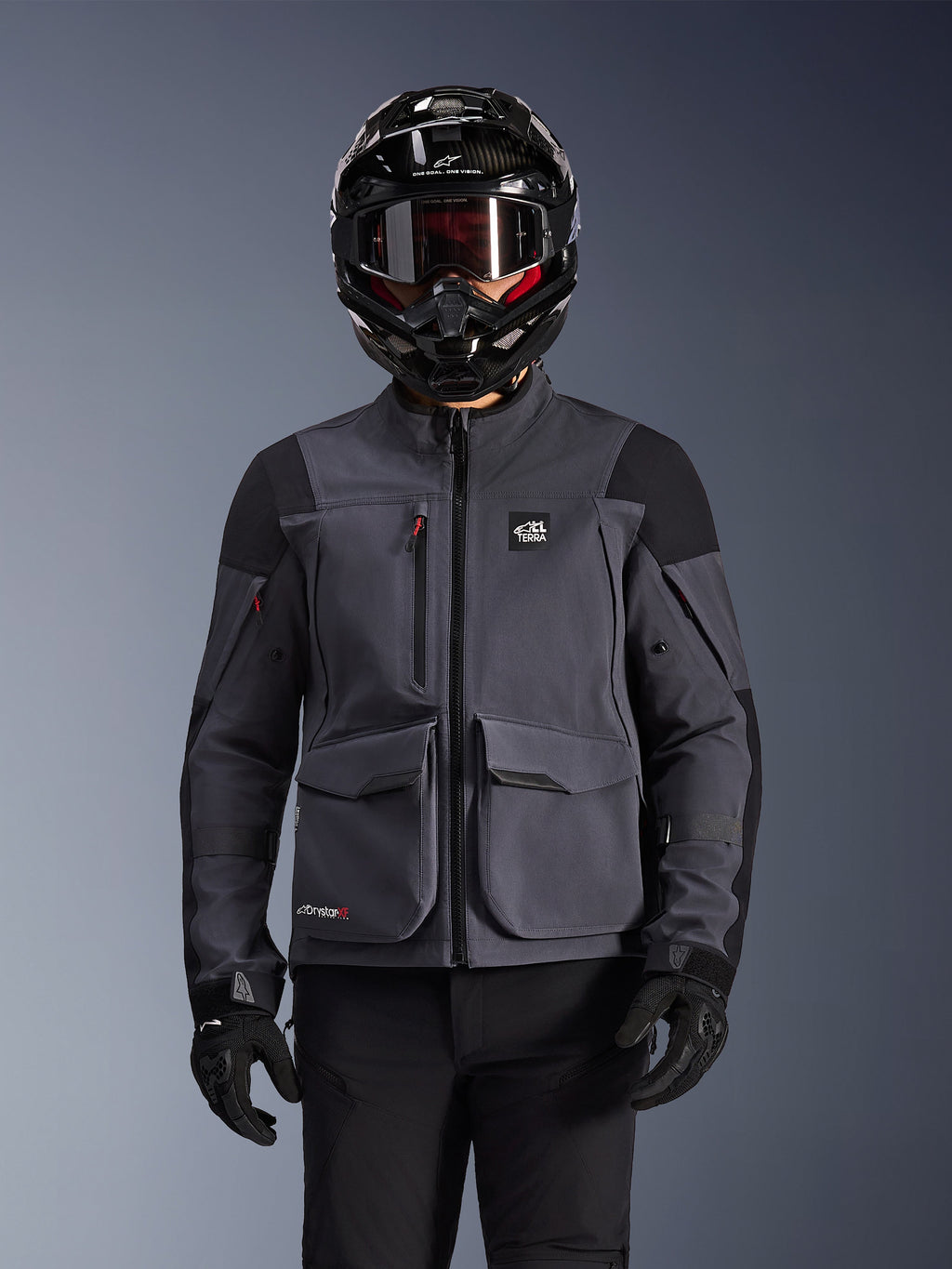 Alpinestars Maxdura Drystar®XF Laminierte Gepanzerte Jacke, Motorradjacke, Dunkelgrau und Schwarz, getragen von einem Fahrer mit schwarzem Helm, Goggles und Handschuhen, mit großen technischen Cargotaschen und ALL TERRA Branding, Adventure-Touring-Ausrüstung