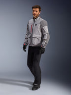 Alpinestars Maxdura Drystar®XF Laminierte Gepanzerte Jacke, Adventure-Motorradjacke, Mittelgrau und Dunkelgrau, getragen von einem Model mit schwarzen Motorradhosen und Handschuhen, mit roten Reißverschluss-Akzenten und Cargotaschen, professionelle technische Allwetter-Ausrüstung für Adventure-Touren