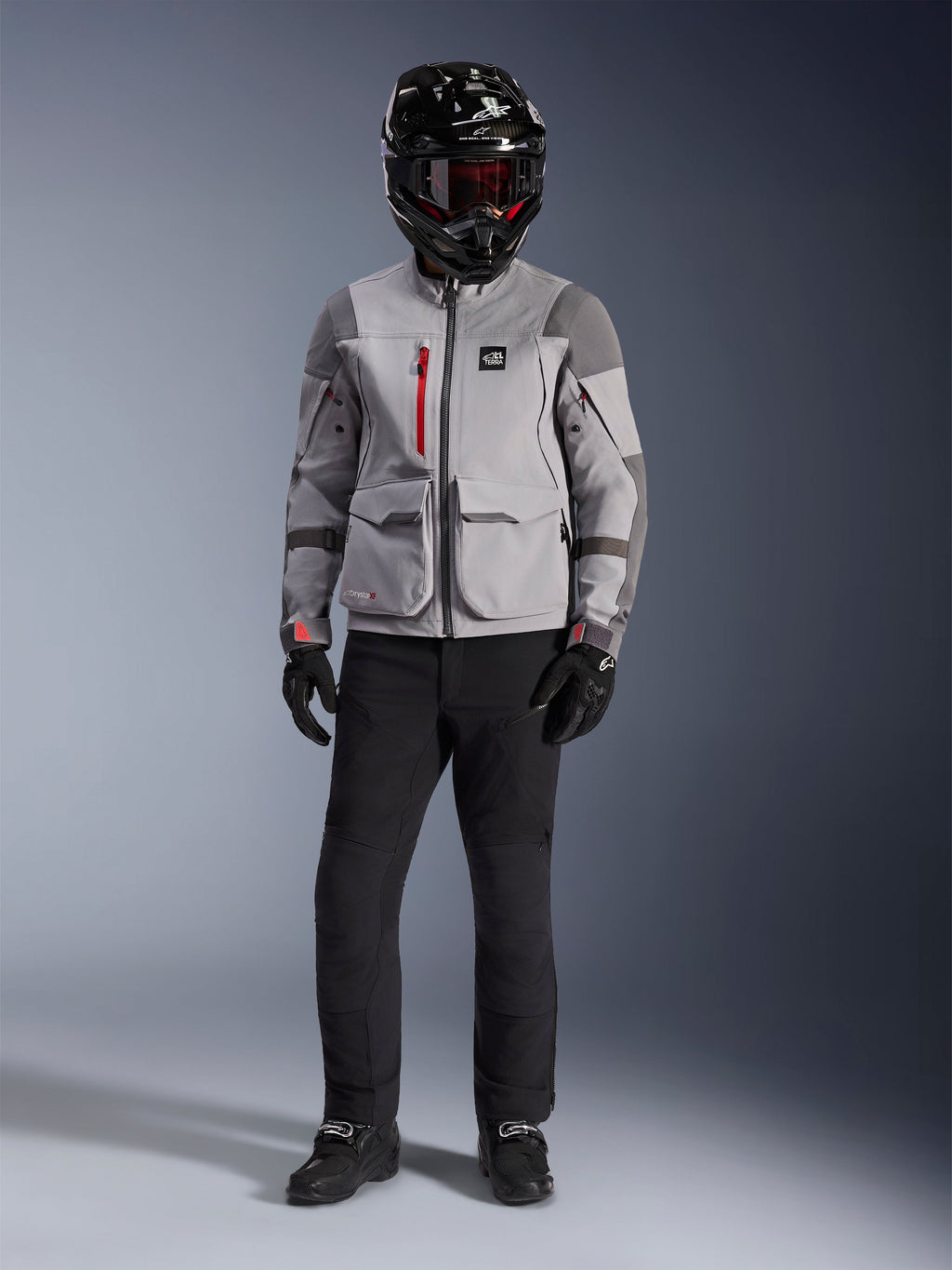 Alpinestars Maxdura Drystar®XF Laminated Armored Shell, Adventure-Jacke in Mittelgrau und Dunkelgrau mit roten Reißverschluss-Akzenten, getragen von einem Fahrer mit schwarzem Helm, roter Brille und schwarzer Hose, professionelle Allwetter-Motorradausrüstung