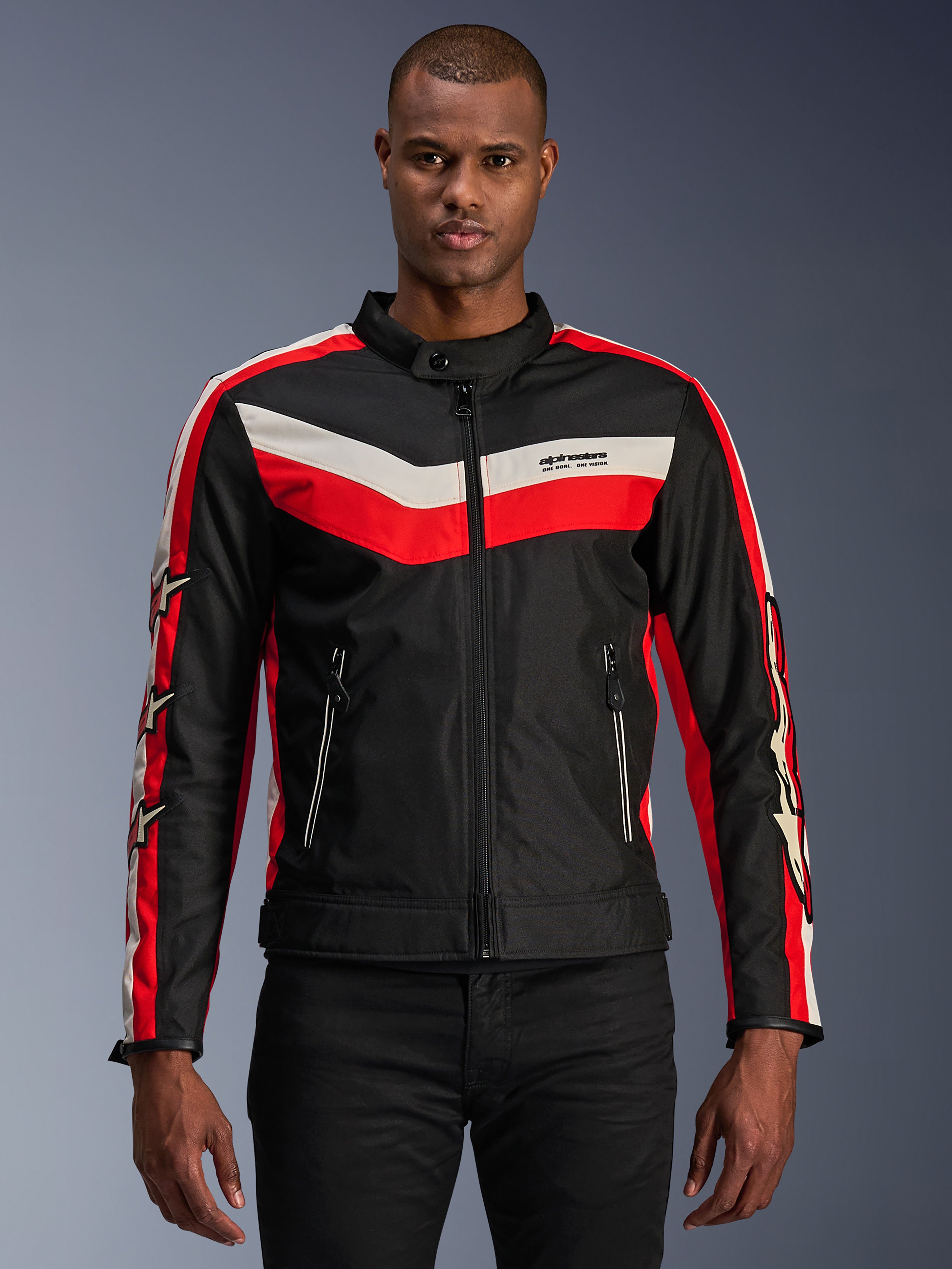 Alpinestars T-Dyno WR Jacke, Textil-Motorradjacke, Schwarz mit leuchtend roten und ecrufarbenen Chevron-Streifen, Vintage-inspirierte Biker-Passform, hoher Kragen mit Knopfverschluss, Reißverschlusstaschen vorne, Sternlogos auf den Ärmeln, von einem Model getragen