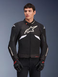 Alpinestars T-GP R V3 Drystar Jacke, wasserdichte Sport-Textiljacke, Schwarz und Weiß mit roten Akzenten, mit einem großen weißen Stern-Logo auf der Brust und weißem Branding auf den Ärmeln, getragen mit schwarz-roten Motorradhandschuhen