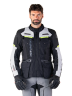 Mann in Alpinestars Bogotá Pro Drystar® Jacke, Schwarz, Ice Gray und Yellow Fluo, Ganzjahres-Adventure-Touring-Motorradjacke, wasserdichtes Design mit mehreren Taschen und vertikalem Branding, kombiniert mit schwarzen Handschuhen und grauer Motorradhose