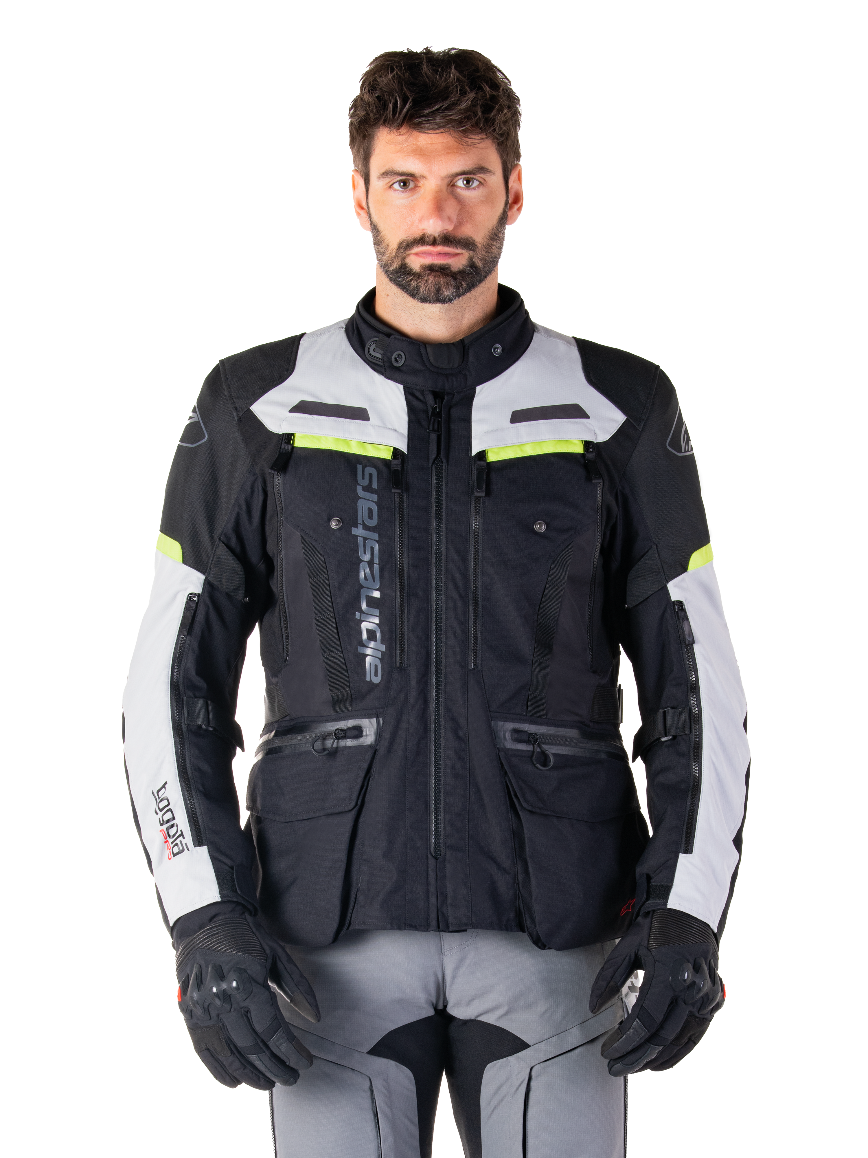 Mann in Alpinestars Bogotá Pro Drystar® Jacke, Schwarz, Ice Gray und Yellow Fluo, Ganzjahres-Adventure-Touring-Motorradjacke, wasserdichtes Design mit mehreren Taschen und vertikalem Branding, kombiniert mit schwarzen Handschuhen und grauer Motorradhose