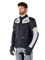 Alpinestars Bogotá Pro Drystar® Jacke, Adventure-Touring-Motorradjacke, Schwarz, Ice Gray und Gelb Fluo, getragen von einem Mann mit passender grauer Hose und schwarzen Handschuhen, mit technischen Belüftungspanelen und Multi-Pocket-Design.