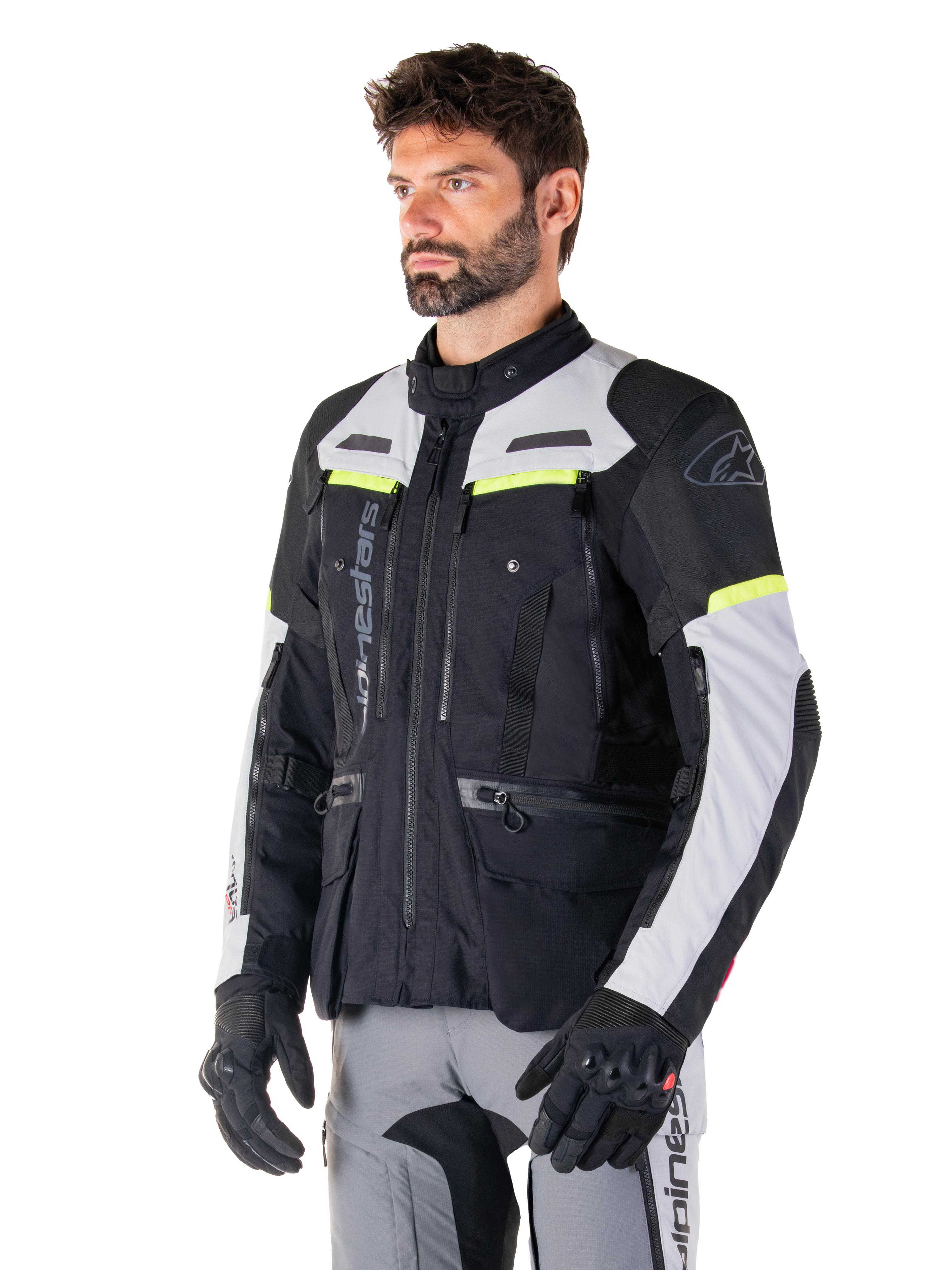 Alpinestars Bogotá Pro Drystar® Jacke, Adventure-Touring-Motorradjacke, Schwarz, Ice Gray und Gelb Fluo, getragen von einem Mann mit passender grauer Hose und schwarzen Handschuhen, mit technischen Belüftungspanelen und Multi-Pocket-Design.