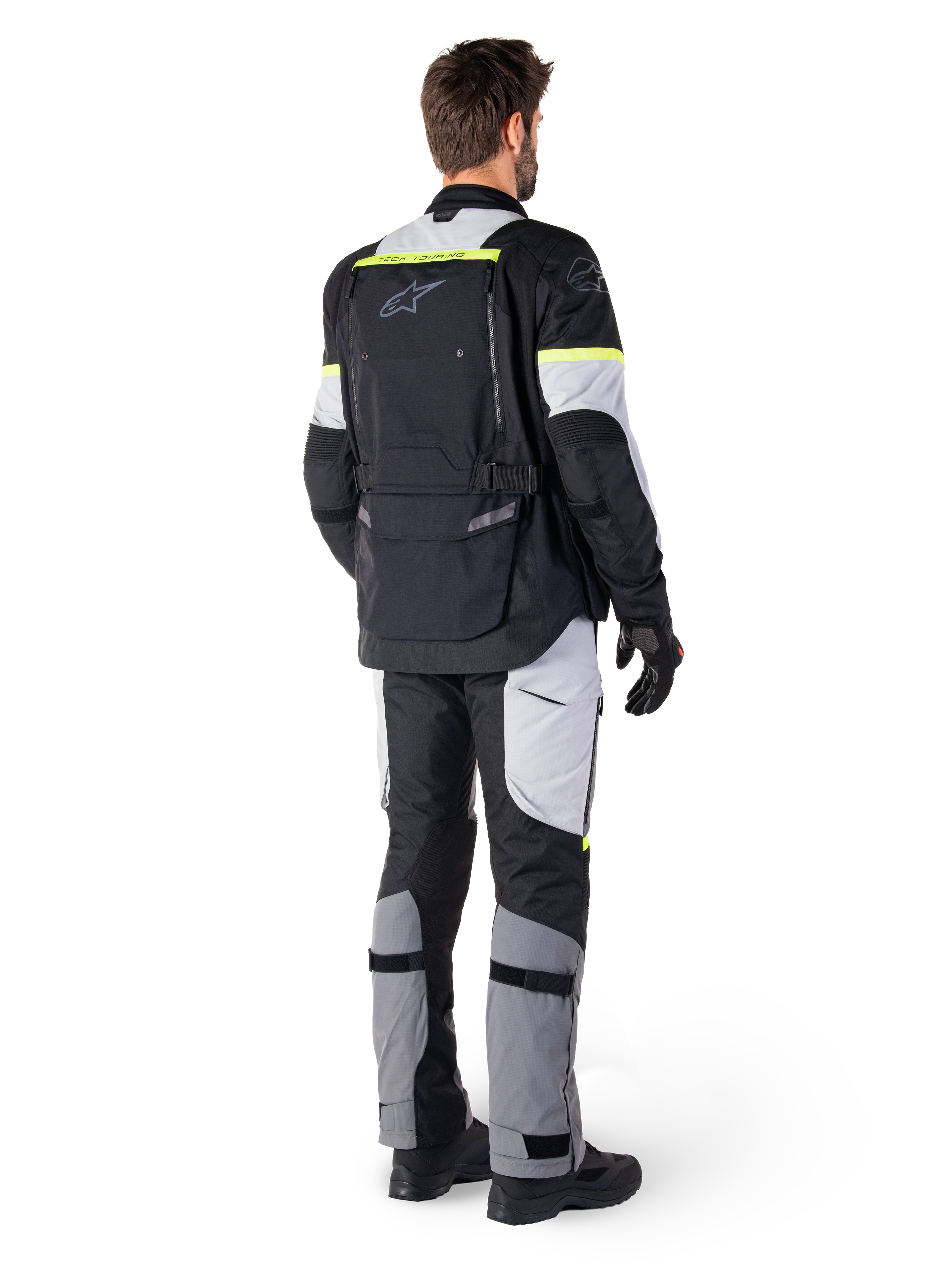 Rückansicht eines Fahrers in der Alpinestars Bogotá Pro Drystar® Jacke in Black Ice Gray Yellow Fluo, kombiniert mit passender Adventure-Tourenhose, mit einer großen Rückentasche und neongelben Akzenten, Ganzjahres-Textil-Motorradausrüstung.