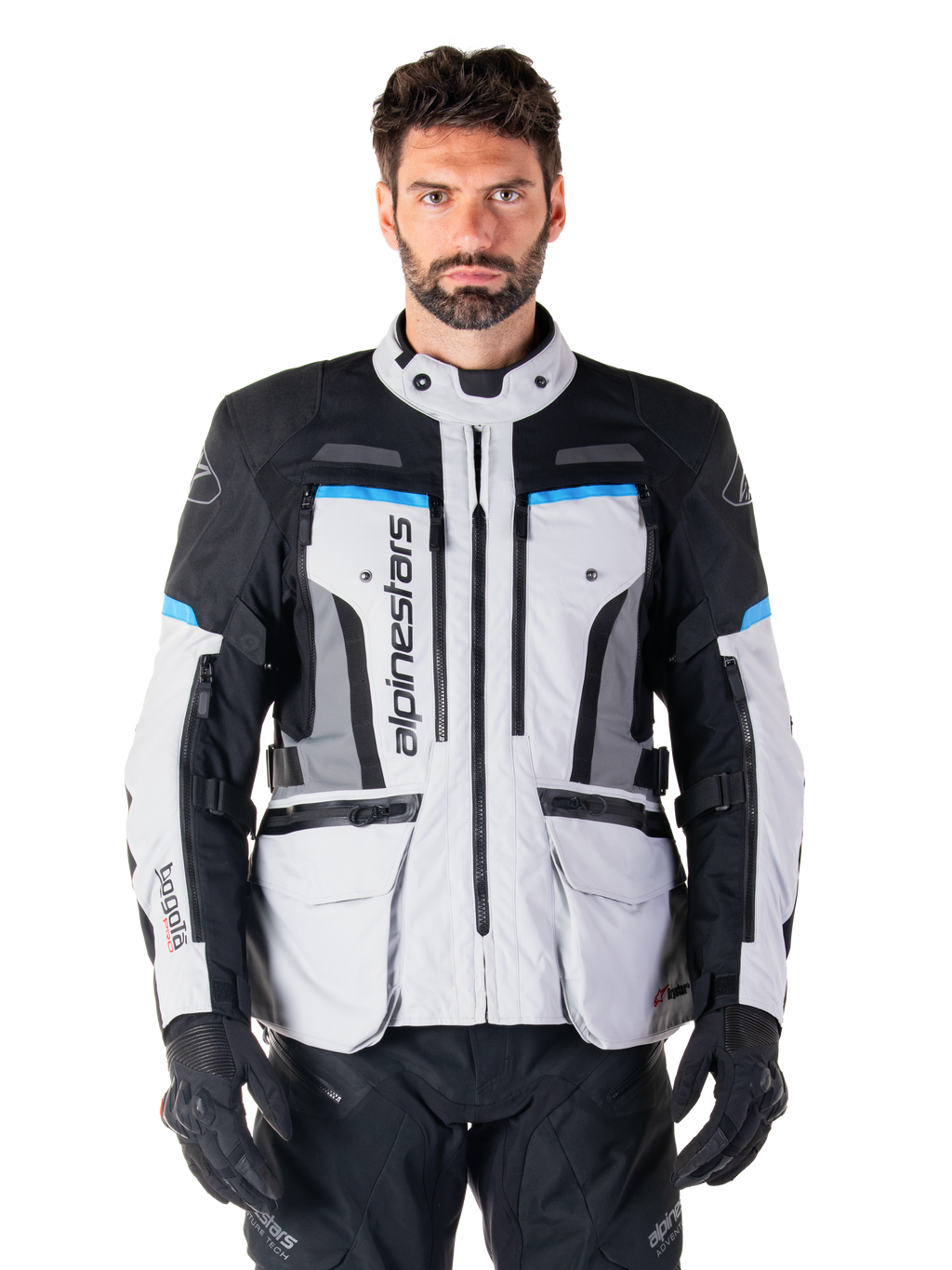 Alpinestars Bogota Pro Drystar Jacke, Motorrad-Adventure-Touringjacke, Eisgrau mit schwarzen und cyanblauen Akzenten, Vorderansicht mit Belüftungspanelen und Cargo-Taschen, getragen von einem Modell mit schwarzer Motorradhose und Handschuhen