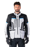 Alpinestars Bogota Pro Drystar Jacke, Motorrad-Adventure-Touringjacke, Eisgrau mit schwarzen und cyanblauen Akzenten, Vorderansicht mit Belüftungspanelen und Cargo-Taschen, getragen von einem Modell mit schwarzer Motorradhose und Handschuhen