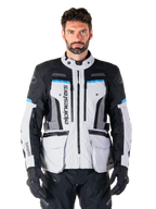 Alpinestars Bogota Pro Drystar Jacke, Motorrad-Adventure-Touringjacke, Eisgrau mit schwarzen und cyanblauen Akzenten, Vorderansicht mit Belüftungspanelen und Cargo-Taschen, getragen von einem Modell mit schwarzer Motorradhose und Handschuhen
