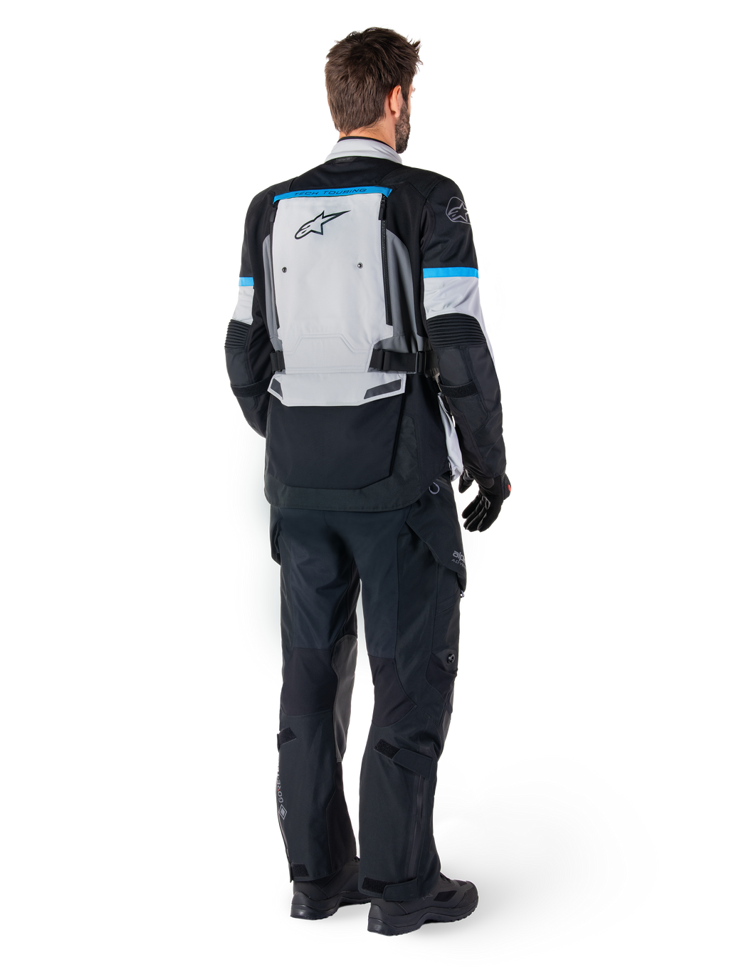 Alpinestars Bogota' Pro Drystar® Jacke, Adventure-Motorradjacke, Ice Gray, Schwarz und Cyan, Rückansicht, getragen mit passender schwarzer Hose und Handschuhen, mit einem großen grauen Rückenteil, schwarzem Alpinestars-Logo und cyanblauen Akzenten.