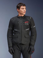 Alpinestars Andes Air Drystar® Jacke, schwarze Motorrad-Tourenjacke, rotes Stern-Logo auf der Brust, mit Mesh-Belüftungseinsätzen und reflektierenden Akzenten, getragen von einem männlichen Model mit schwarzen Motorradhandschuhen, Adventure-Ausrüstung für zwei Jahreszeiten