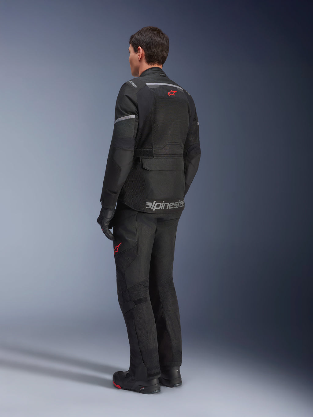 Alpinestars Andes Air Drystar® Jacke, Schwarz, Rückansicht eines Fahrers, mit großflächigen Mesh-Einsätzen zur Belüftung, getragen mit passender Adventure-Motorradhose und -stiefeln, präsentiert das straßenorientierte Touring-Design und Branding.
