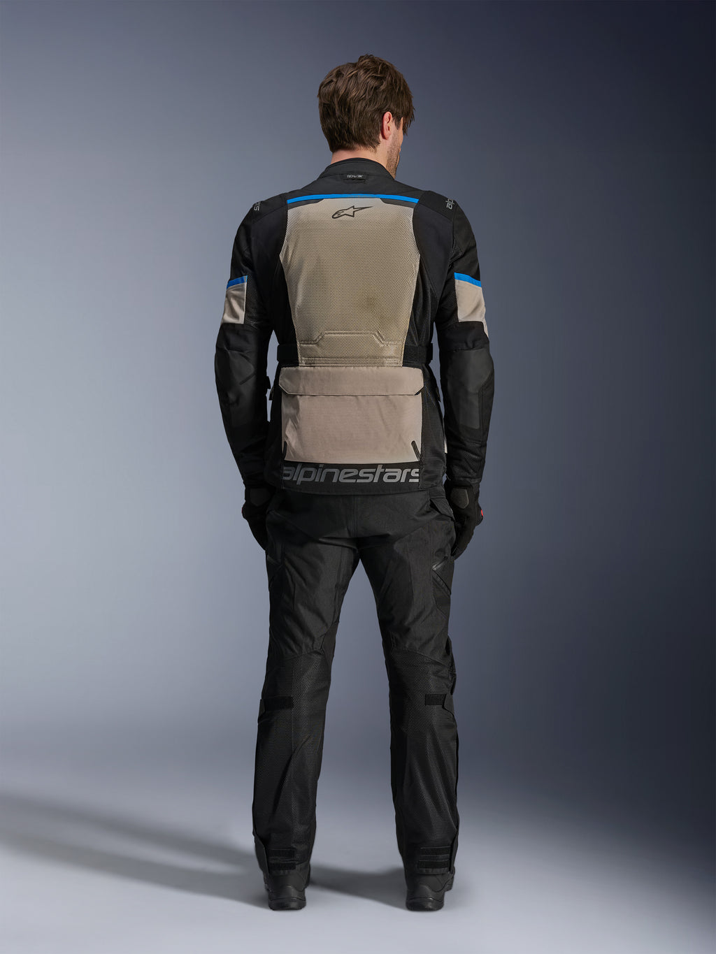Alpinestars Andes Air Drystar® Jacke, Black Laurel Gray Bright Blue, Rückansicht mit großem Mesh-Belüftungspanel, große Aufbewahrungstasche am unteren Rücken mit Alpinestars-Branding, technische Motorrad-Tourenjacke getragen mit passender Hose.