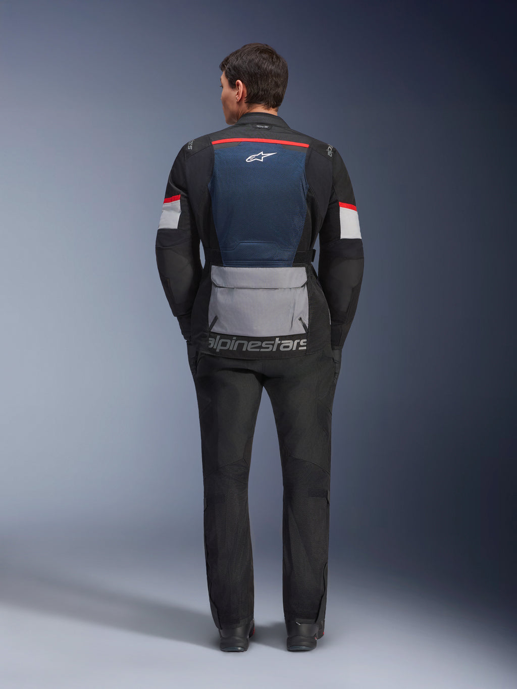 Alpinestars Andes Air Drystar Jacke, Deep Blue Black Ice Gray, Rückansicht am Model, mit blauem Mesh-Rückeneinsatz zur Belüftung, großer grauer Tasche im unteren Bereich, roten und weißen Akzenten an den Ärmeln, „alpinestars“-Schriftzug, kombiniert mit schwarzer Motorradhose für ein komplettes Touren-Outfit