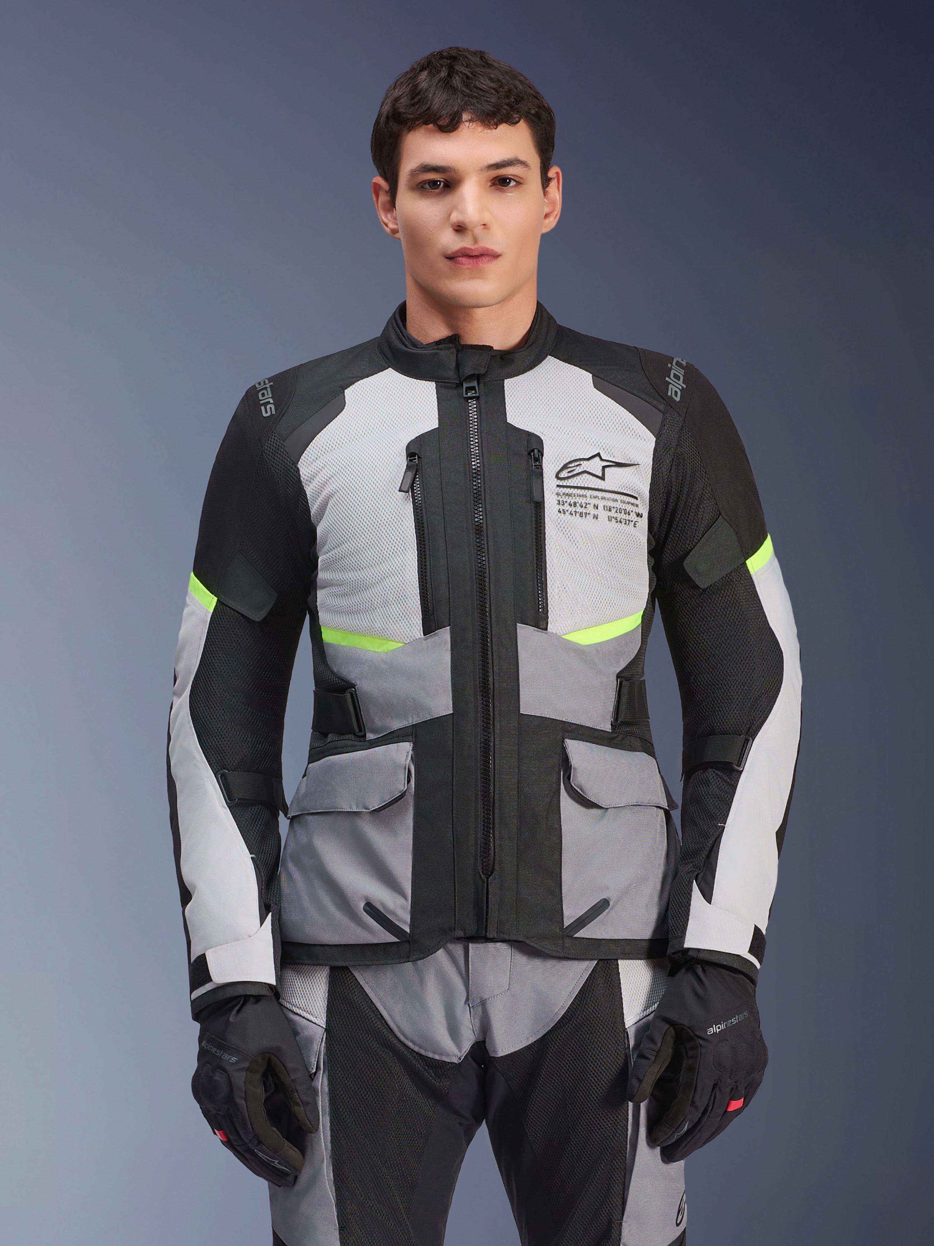 Männlicher Fahrer trägt die Alpinestars Andes Air Drystar® Jacke in Ice Gray, Dunkelgrau und Schwarz, mit neongelben Akzenten und Mesh-Belüftungseinsätzen, kombiniert mit passender Motorradhose und Handschuhen, Adventure-Touring-Ausrüstung