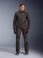 Motorradfahrerin mit Alpinestars Stella Andes V4 Drystar® Jacke in Schwarz, kombiniert mit passender schwarzer Adventure-Tourenhose und Handschuhen, technische Textilkonstruktion mit mehreren Funktionstaschen und weißem Alpinestars-Branding, komplette Allwetter-Motorradausrüstung