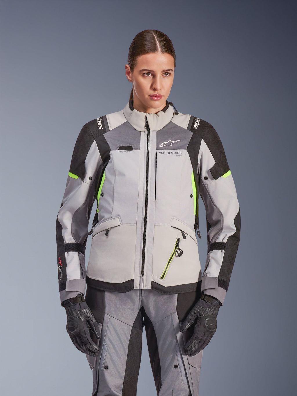 Alpinestars Stella Andes V4 Drystar® Damenjacke, Eisgrau und Dunkelgrau mit neongelben Akzenten, Adventure-Touring-Motorradjacke, getragen mit passender Hose und Handschuhen, schützende Textilkonstruktion mit Alpinestars-Branding.