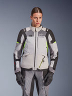 Alpinestars Stella Andes V4 Drystar® Damenjacke, Eisgrau und Dunkelgrau mit neongelben Akzenten, Adventure-Touring-Motorradjacke, getragen mit passender Hose und Handschuhen, schützende Textilkonstruktion mit Alpinestars-Branding.