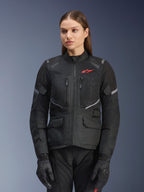 Alpinestars Stella Andes Air Drystar Jacke, Damen-Motorrad-Tourenjacke, Schwarz mit grauen Akzenten und einem kleinen roten Logo, mit Mesh-Belüftungseinsätzen, einem hohen Kragen und mehreren Funktionstaschen, getragen mit passenden Motorradhandschuhen und -hosen
