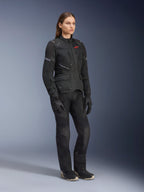 Frau in Alpinestars Stella Andes Air Drystar® Jacke, schwarze Textil-Adventure-Tourenjacke, kombiniert mit passender schwarzer Hose und Handschuhen, mit großen Mesh-Belüftungseinsätzen und rotem Logo, abgestimmtes Outfit für Motorradfahrerinnen