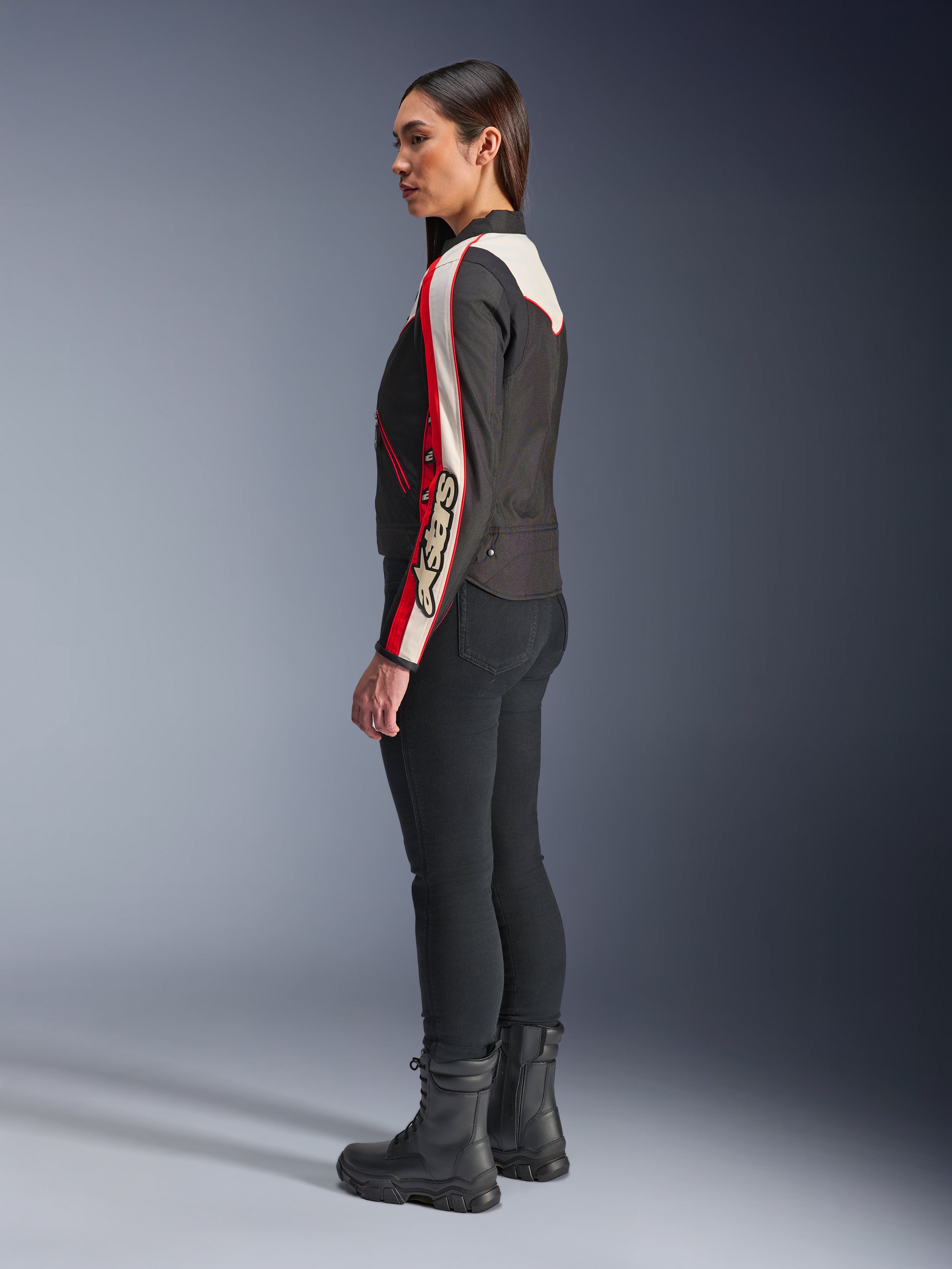 Alpinestars Stella T-Dyno WR Jacke, Damen-Textilmotorradjacke, Schwarz, Ecru und Hellrot, Vintage-inspiriertes Design mit Astars-Branding am Ärmel, getragen mit schmaler schwarzer Hose und schwarzen Stiefeln, kurzer Biker-Schnitt für urbane Straßenfahrten