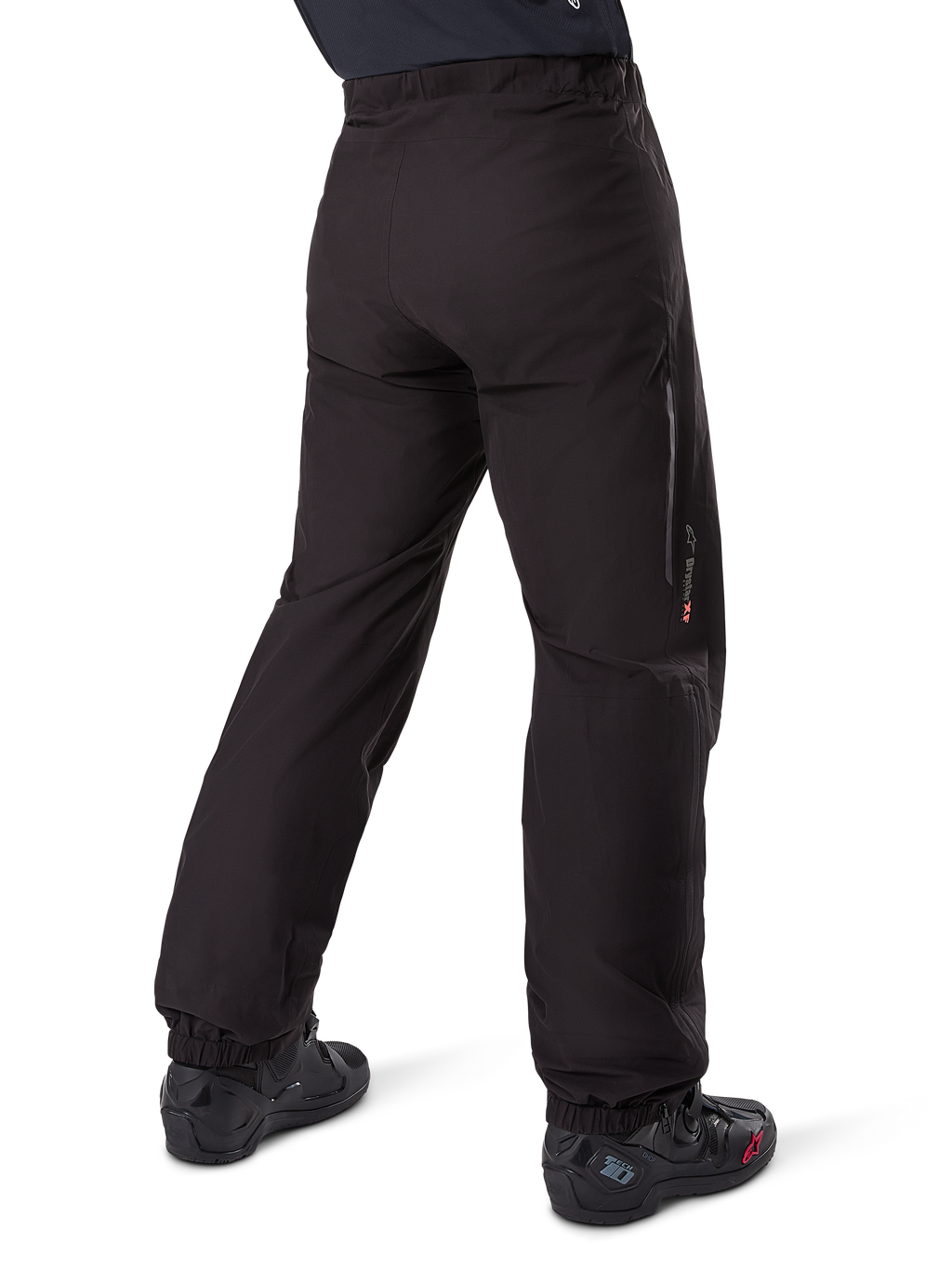 Alpinestars Amt-8 Stretch Drystar® XF Hosen-Innenfutter, Schwarz, Rückansicht zeigt das wasserdichte Futter über schwarzen Motorradstiefeln getragen, mit Drystar XF Branding am Unterschenkel, elastischen Knöchelbündchen und leichtem Stretchmaterial für Adventure-Touren.