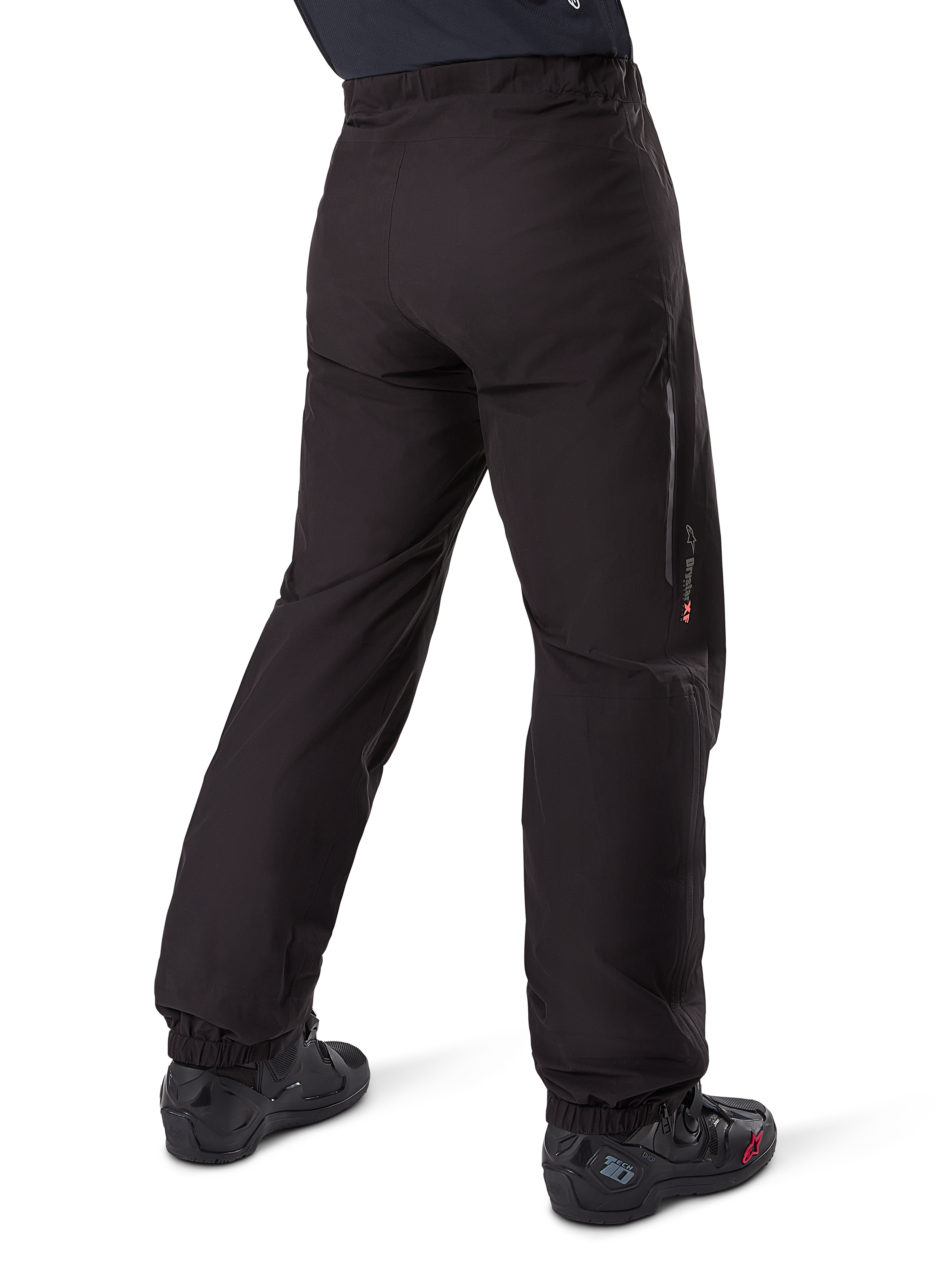 Alpinestars Amt-8 Stretch Drystar® XF Hosen-Innenfutter, Schwarz, Rückansicht zeigt das wasserdichte Futter über schwarzen Motorradstiefeln getragen, mit Drystar XF Branding am Unterschenkel, elastischen Knöchelbündchen und leichtem Stretchmaterial für Adventure-Touren.