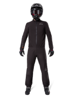 Motorradfahrer in Alpinestars AMT-8 Stretch Drystar® XF Hosenfutter und passender Jacke, komplett schwarze wasser- und winddichte technische Ausrüstung, schwarzer Helm, Handschuhe und Stiefel, schlankes Adventure-Touring-Design.