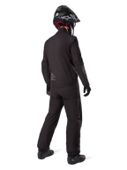 Rider from behind wearing Alpinestars Amt 8 Stretch Drystar® XF liner and pants, all-black technical adventure gear, waterproof and windproof stretch material, matching jacket with 'AMT' branding, black helmet, and boots for a complete all-weather motorcycle touring outfit