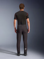 Alpinestars Aeroshell Hose, Crossover-Sport-Softshell-Motorradhose, Schwarz, Rückansicht kombiniert mit einem schwarzen kurzärmeligen Base-Layer, schmale Passform, vorgeformte Knie, weißes Astars-Logo am unteren linken Bein.