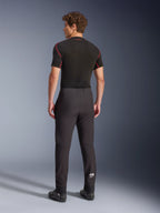Alpinestars Aeroshell Hose, Schwarz, Softshell-Motorradhose, Rückansicht an einem Model, moderne schmal zulaufende Passform, weißes Astars-Logo am Unterschenkel, elastische Säume, kombiniert mit einem schwarzen kurzärmeligen Base Layer und Motorradschuhen.