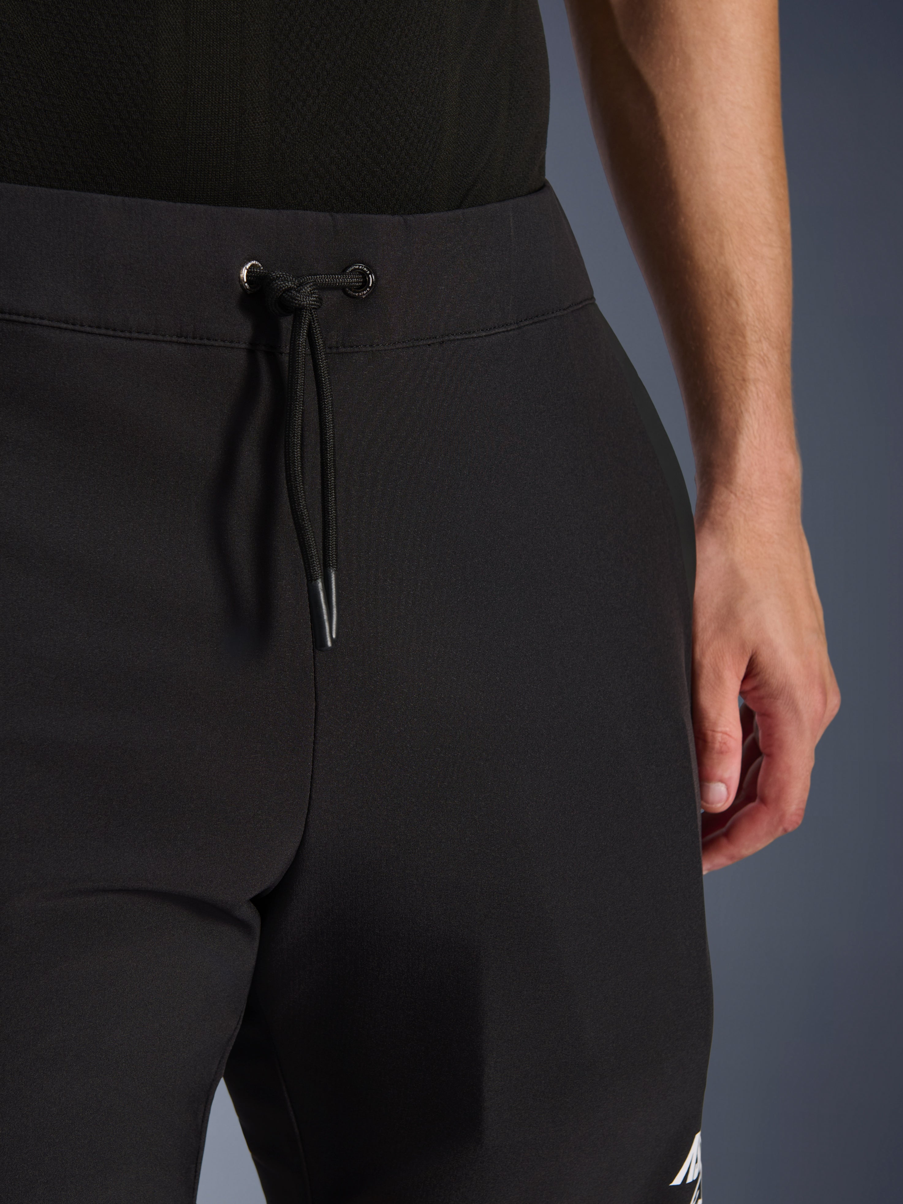 Alpinestars Aeroshell Hose, schwarze Softshell-Motorradhose, Nahaufnahme des elastischen Bunds und Kordelzugverschlusses, modernes minimalistisches Design, strapazierfähige Textilkonstruktion für Freizeit-Touring