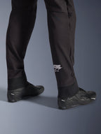 Alpinestars Aeroshell Hose, schwarze Softshell-Motorradhose, Nahaufnahme des Unterschenkels und des elastischen Saums, weißes Alpinestars-Logo an der Wade, kombiniert mit schwarzen Motorradschuhen, modernes Crossover-Sport-Design