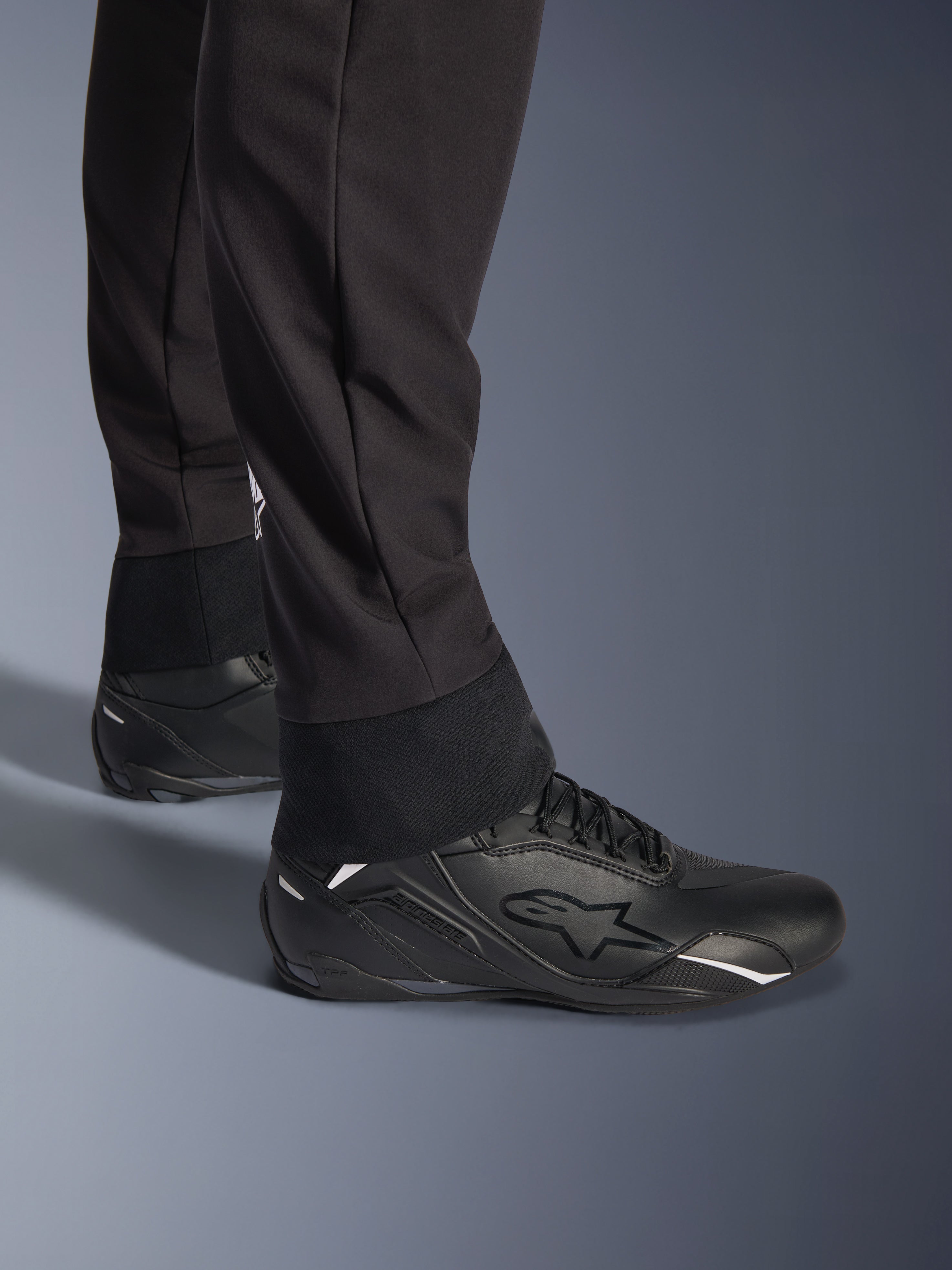 Alpinestars Aeroshell Hose, Schwarz, Nahaufnahme des elastischen unteren Saums und Bündchens, modernes Sport-Softshell-Design, getragen mit schwarzen Alpinestars Motorradschuhen