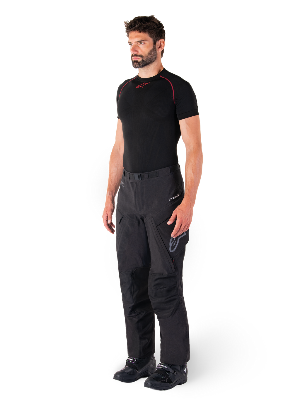 Alpinestars Hyde XT Drystar® Hose, schwarze Adventure-Touring-Motorradhose, getragen von einem Model mit einem schwarzen Kompressionsshirt und schwarzen Stiefeln, technische wasserdichte Konstruktion und Drystar®XF-Branding.