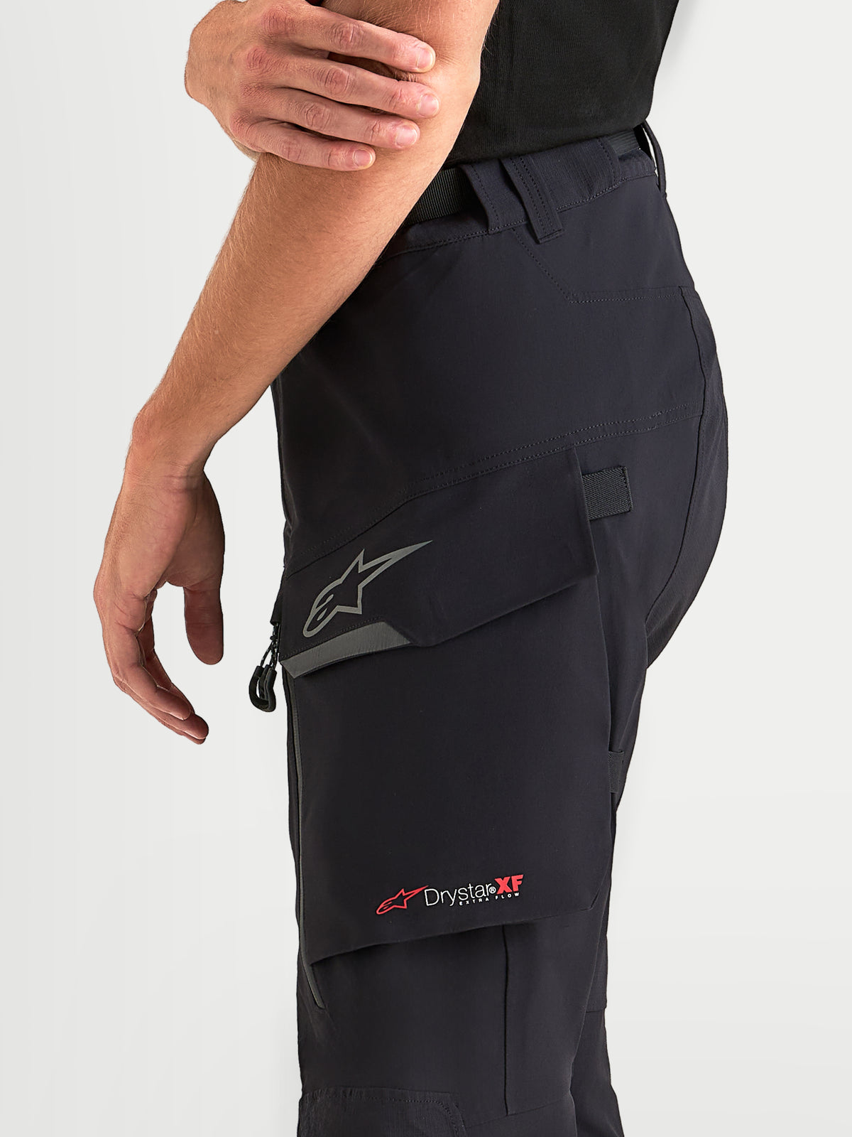 Alpinestars Maxdura Drystar XF laminierte Hose, Herren-Adventure-Motorradhose in Schwarz und Dunkelgrau, getragen von Model, Nahaufnahme der wasserabweisenden Beintasche mit reflektierendem Astar-Logo und Drystar XF-Branding