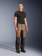 Alpinestars Andes V4 Drystar® Hose, Motorrad-Adventure-Touring-Hose, Walnut Black mit orangefarbenen Akzenten, getragen von einem Model mit schwarzem Kurzarm-Baselayer und schwarzen Stiefeln, verstärkte Textileinsätze und Cargotaschen, robustes Design für Fahrten bei jedem Wetter