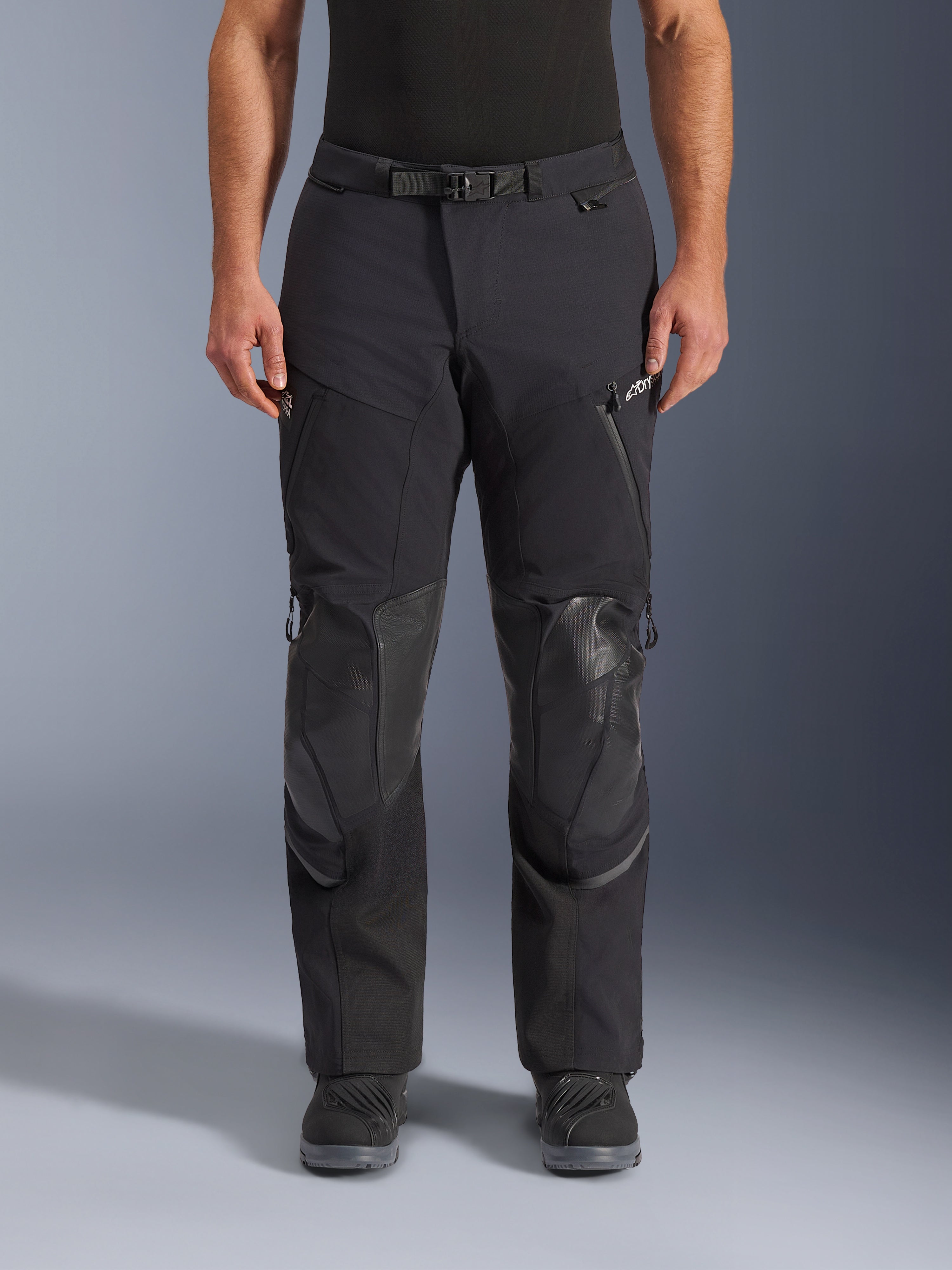 Alpinestars Andes Pro Drystar® XF Hose, Adventure-Touring-Motorradhose in Black Dark Gray, Frontansicht, mit 3-lagiger Laminatkonstruktion, integrierten Knieprotektoren, wasserdichten Reißverschlusstaschen und magnetischem Bundverschluss, kombiniert mit schwarzen Motorradstiefeln.
